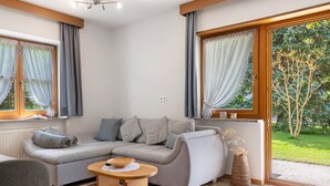 Un salon moderne avec un canapé d’angle, une petite table en bois et une vue sur un jardin grâce à de grandes fenêtres.