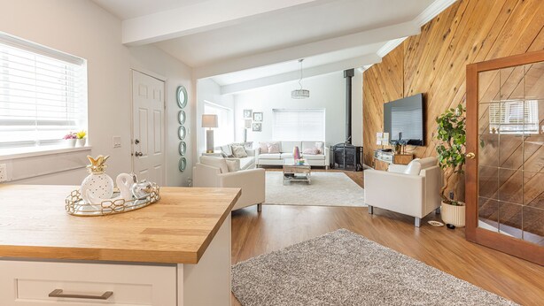 Ein modernes Wohnzimmer mit Holzboden, weißen Sofas, einem Couchtisch und einem an der Wand befestigten Fernseher.