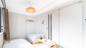 Camera d'albergo compatta con un letto, un tavolino con bollitore, un lampadario e un armadio con ante scorrevoli.