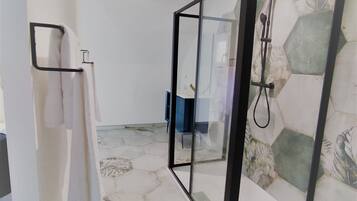 A bathroom with a glass-enclosed shower, a white towel rack, and a tiled floor with a geometric pattern.