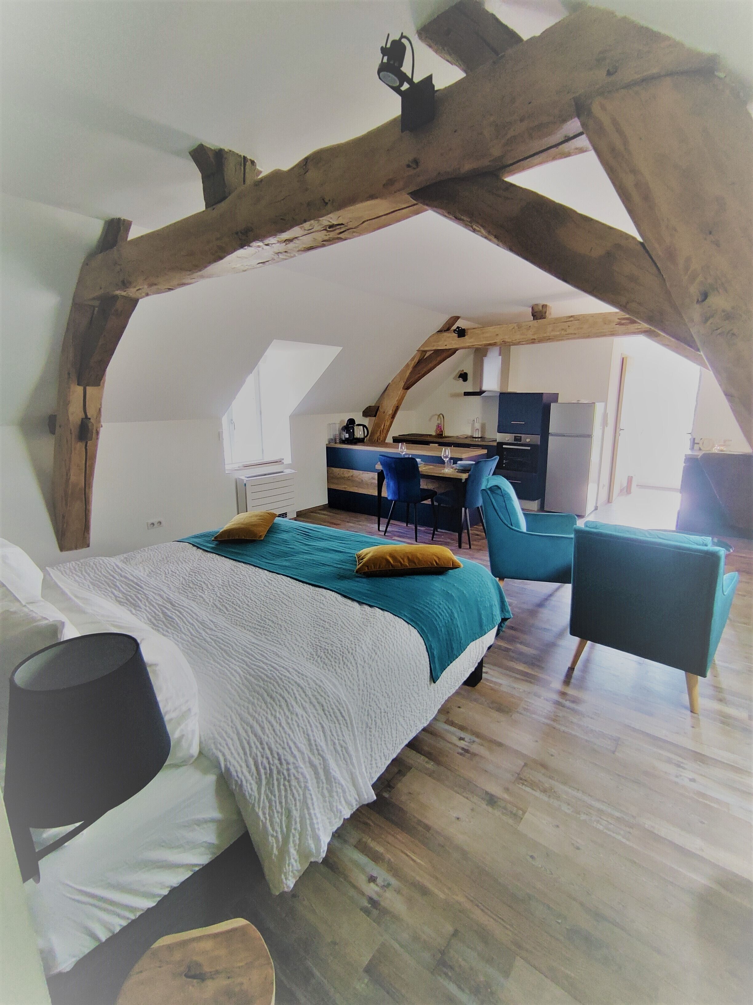 A bedroom with a large bed, a desk, and a chair in a loft-style room with exposed wooden beams.