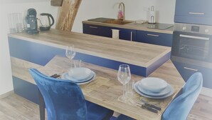A dining area with a wooden table, blue chairs, and a kitchen in the background.