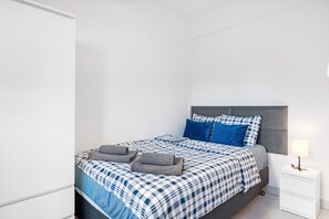 Una cama bien hecha con colcha a cuadros, dos almohadas y dos toallas dobladas.