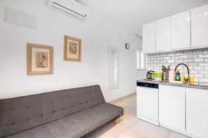 Una cocina moderna con gabinetes blancos, un sofá gris y dos cuadros en la pared.