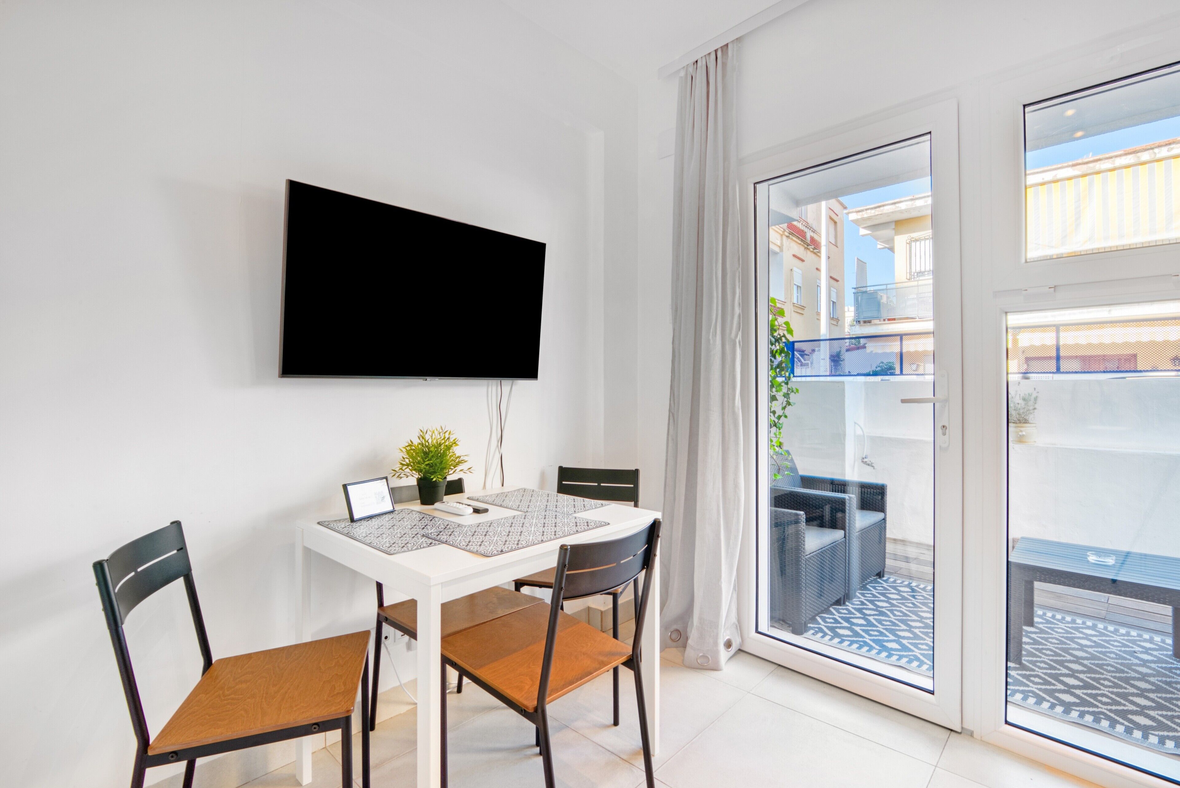 Quarto moderno com televisão de tela plana na parede, mesa de jantar com cadeiras e porta de vidro deslizante para área externa.
