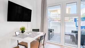 A modern room with a flat-screen TV, a dining table with chairs, a potted plant, and a sliding glass door leading to an outdoor area with a patterned floor. - Holiday Apartment "Soleole1" with Shared Terrace & Wi-Fi (Gandia)