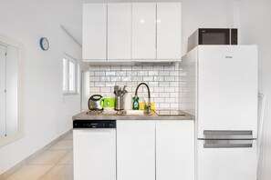 Una cucina con mobili bianchi, lavastoviglie, forno a microonde e lavello con diversi utensili.