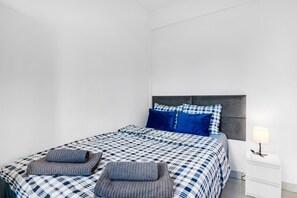Um quarto com cama, almofadas, mesa de cabeceira e abajur.