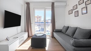 A modern living room with a flat-screen TV, a grey sofa, a white entertainment unit, and a balcony with a view of buildings. - Holiday Apartment "Soleole8" with Shared Terrace, A/C & Wi-Fi (Gandia)