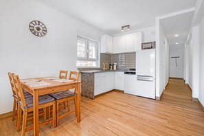 Une cuisine moderne avec des meubles blancs, une table à manger en bois et une horloge au mur.