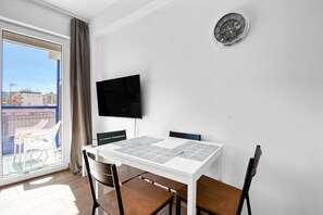 A modern room with a white table, chairs, a flat-screen TV, and a clock on the wall.