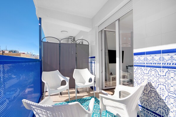 A balcony with white wicker chairs, a blue patterned floor, and a view of the cityscape.