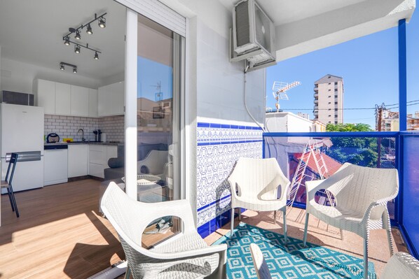 A balcony with white wicker chairs, a patterned table, and a view of buildings.