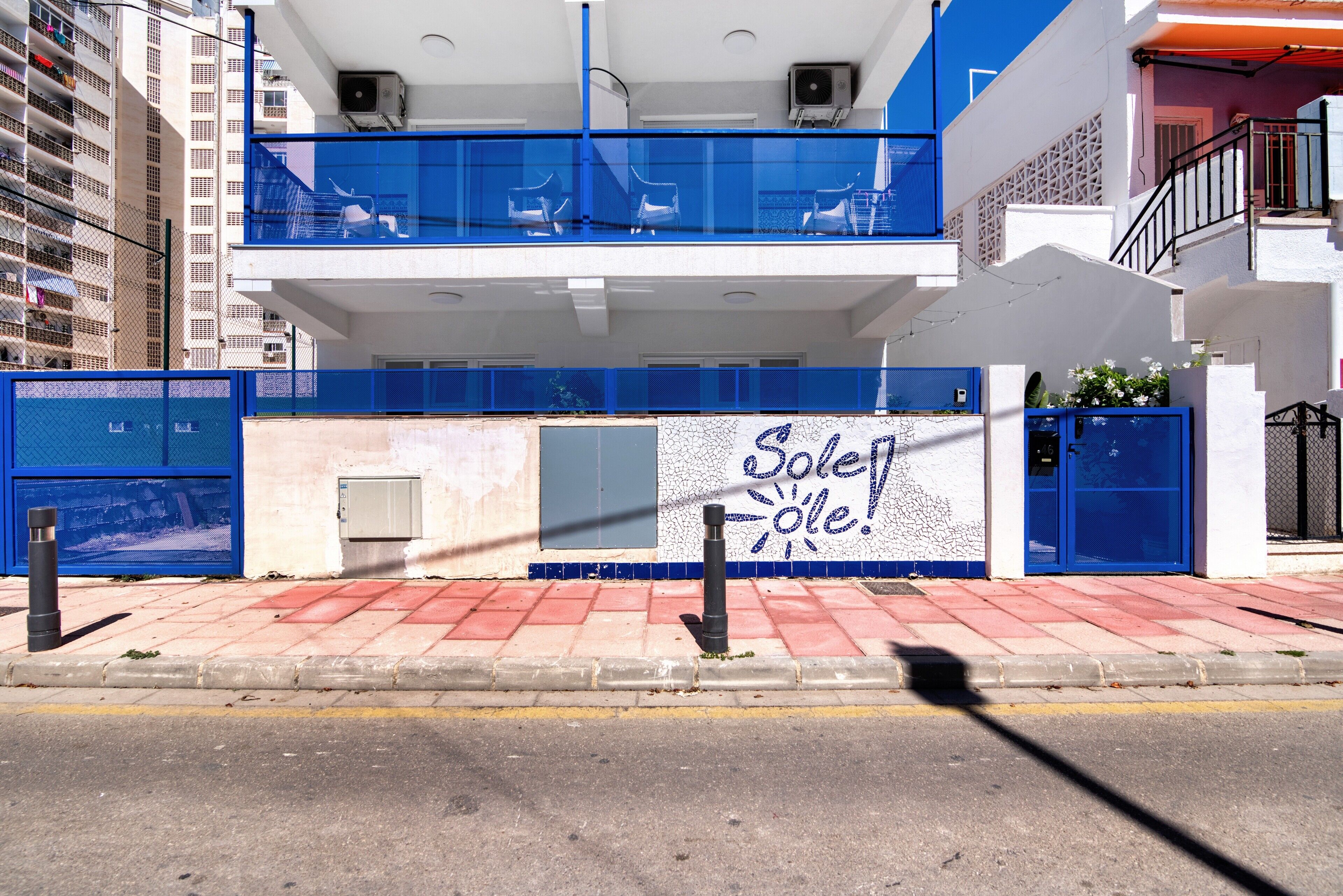 Un immeuble à la façade bleue et blanche, doté d’un balcon avec des chaises et d’une enseigne sur laquelle on peut lire : « Soleil Soleil ! »
