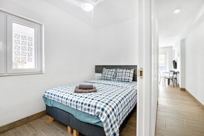 Un dormitorio con una cama, una ventana con diseño geométrico y un pasillo que lleva a un comedor.