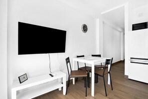 Un comedor moderno con una mesa blanca, sillas negras, un banco blanco, un televisor de pantalla plana en la pared y un reloj.