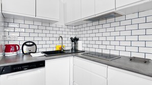 Une cuisine avec des meubles blancs, un lave-vaisselle, une bouilloire rouge et une bouilloire noire posées sur le plan de travail.