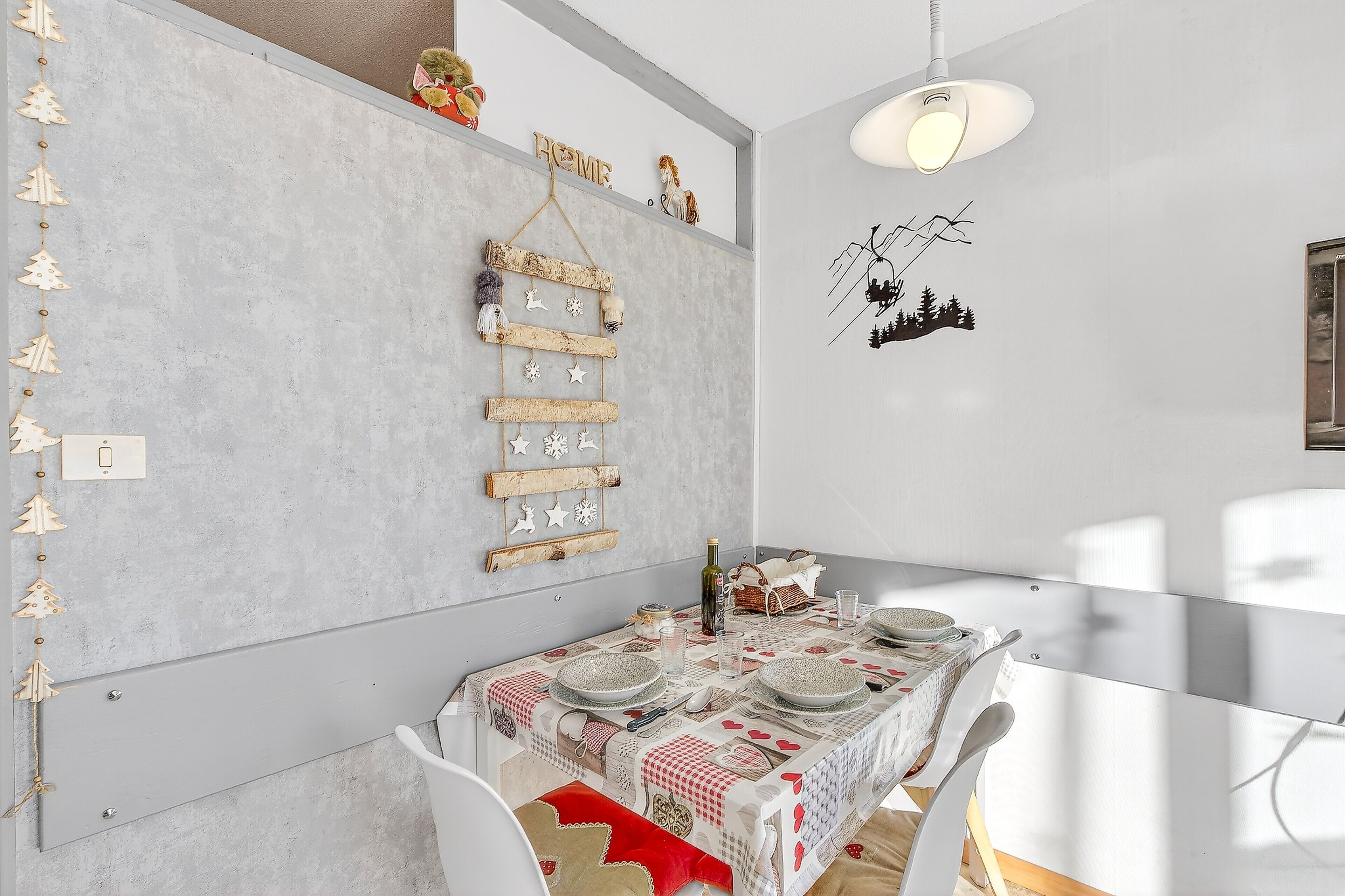 Un coin repas avec une table dressée pour quatre personnes, une décoration suspendue et un luminaire fixé au mur.
