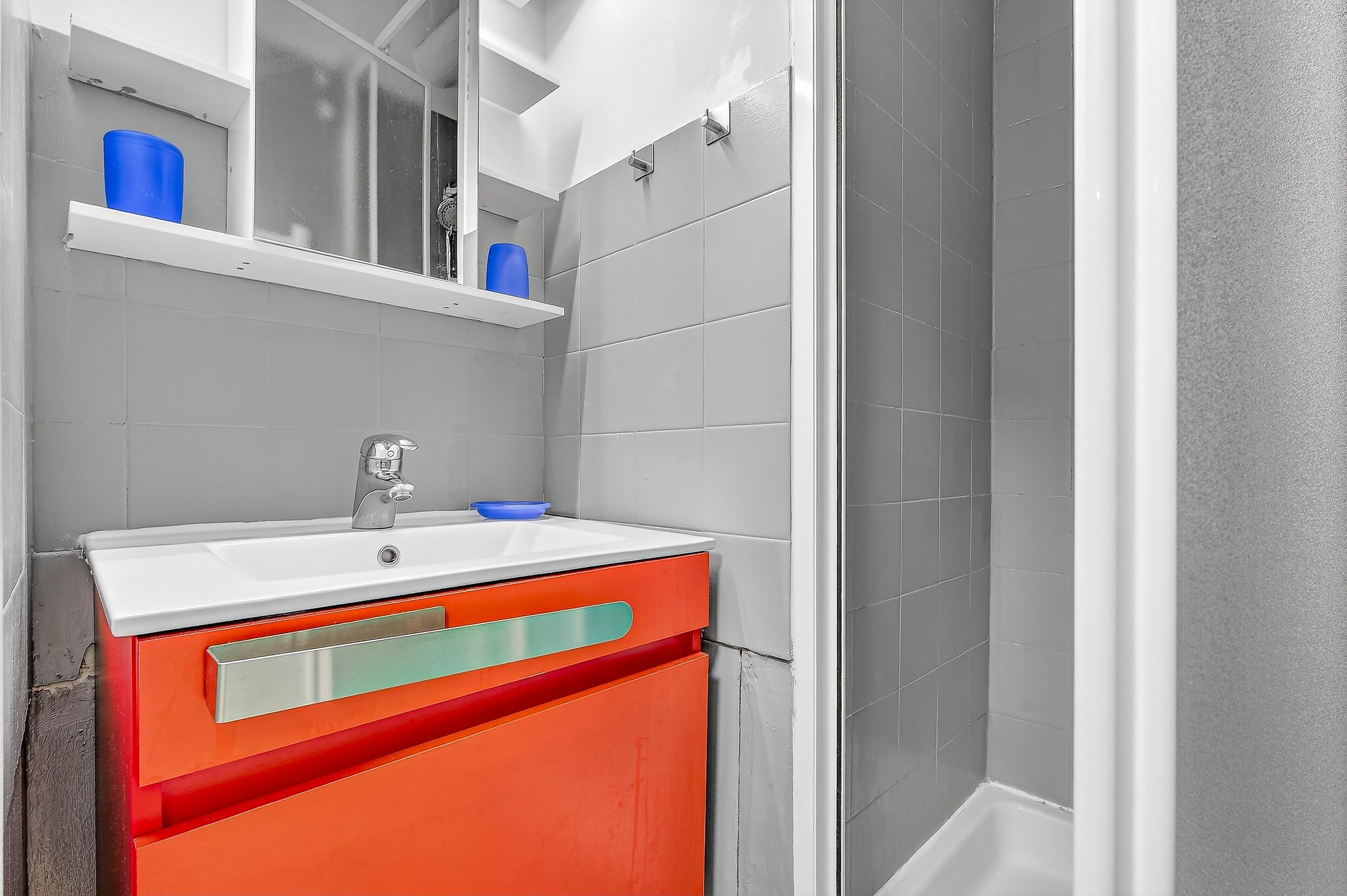 Une salle de bain avec un lavabo blanc, un miroir et un meuble rouge.
