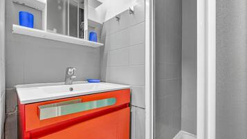 Une salle de bain avec un lavabo blanc, un miroir et un meuble rouge.