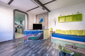 Una sala de estar con un sofá, una mesa de centro de vidrio, un televisor y una pared decorada con un cuadro.