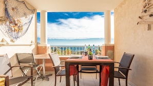 Un coin repas avec une table dressée pour deux personnes, des chaises, une bouteille de vin et une vue sur la mer.