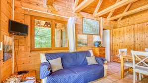 L’intérieur d’un chalet en bois, avec un canapé, une table, des chaises, un téléviseur et une fenêtre.
