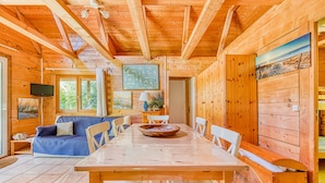 L’intérieur d’un chalet en bois comprend une table à manger, des chaises, un canapé, un téléviseur et un tableau accroché au mur.