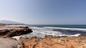 Une plage rocheuse avec des vagues, une montagne lointaine et un ciel dégagé.