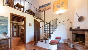 Un escalier avec des finitions en bois et des rampes en métal, une cheminée avec un manteau en pierre et un coin repas agrémenté d’un tapis rouge.