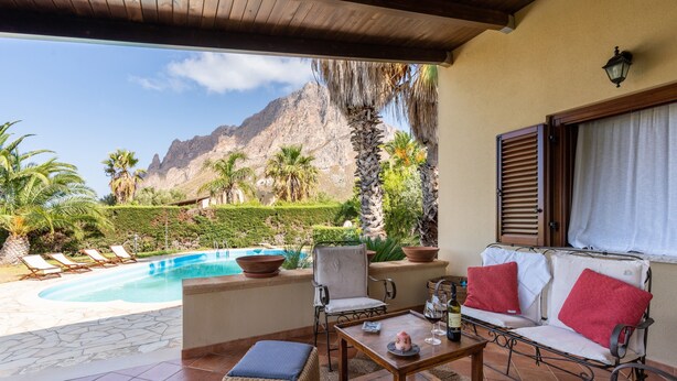 Une terrasse avec une piscine, des chaises longues, une table avec du vin et une vue sur les montagnes.