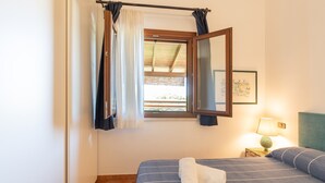 Une chambre à coucher avec un lit, une fenêtre avec des rideaux, une lampe de chevet et un tableau encadré au mur.