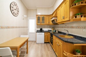 A kitchen with wooden cabinets, a dishwasher, a sink, and a clock on the wall.