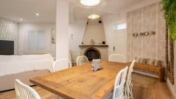 Un comedor con mesa de madera, sillas blancas, chimenea y una planta colgante.