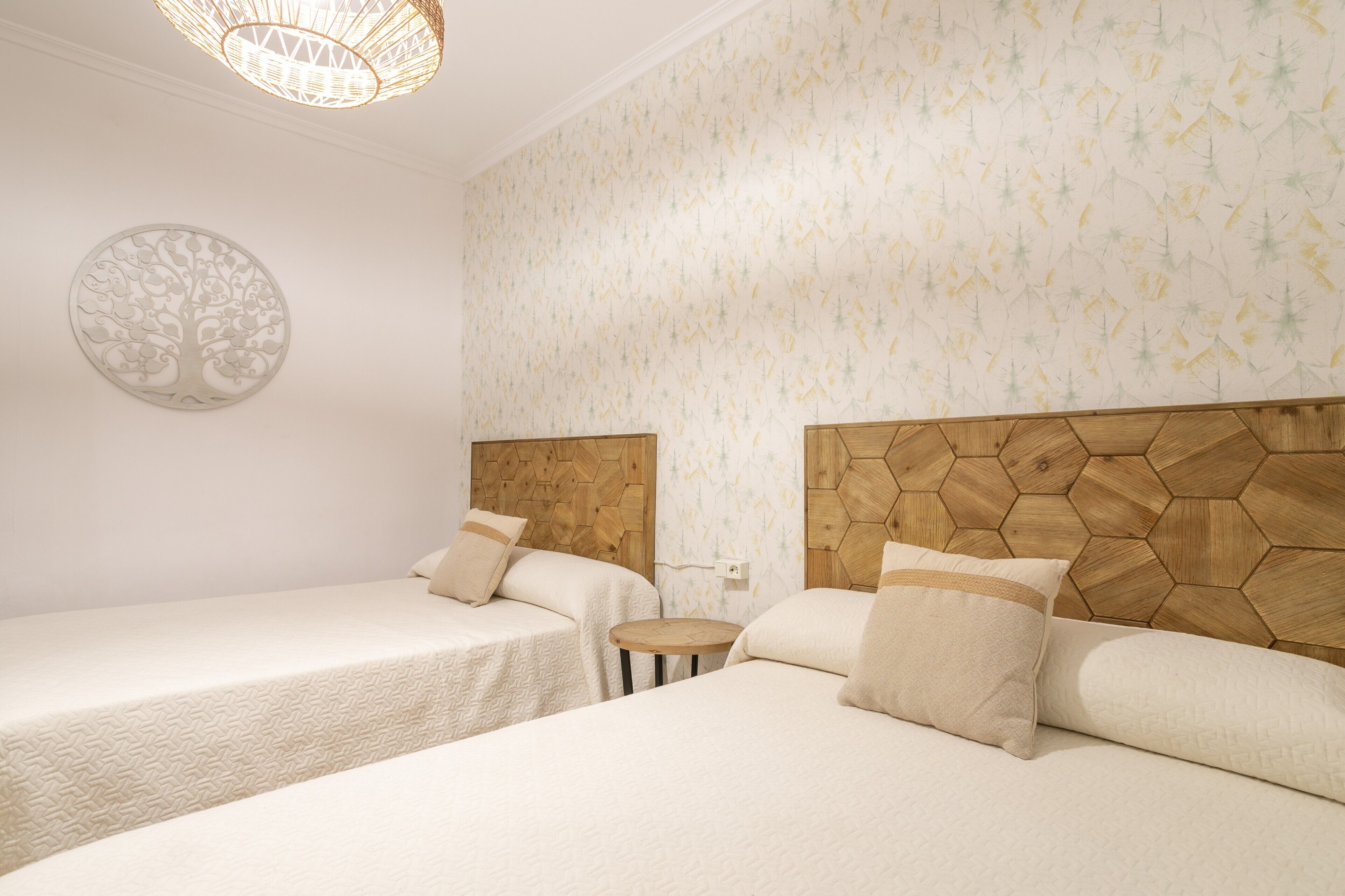 Une chambre avec deux lits, un élément de décoration murale rond, un papier peint à motifs et une tête de lit en bois.