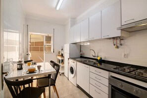 Une cuisine compacte avec des meubles blancs, une cuisinière à gaz, un lave-linge et un coin repas comprenant des chaises et une table.