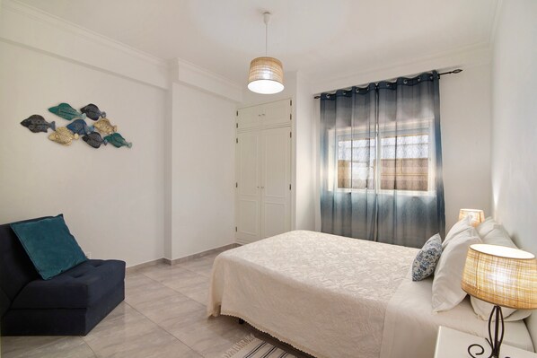 Une chambre à coucher comprenant un lit, une table de chevet, une lampe, une chaise, une armoire et des œuvres d’art murales.