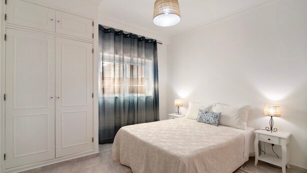 A bedroom with a bed, bedside tables, a wardrobe, and a window with curtains. - Apartment 'Âncora B' with Private Terrace (Monte Gordo)