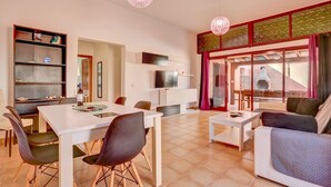 A modern living room with a dining area, white furniture, a TV, and a balcony with a grill. - Villa Malva: Private Jacuzzi, Ping Pong & Relaxation in Corralejo (Corralejo)