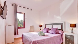 A bedroom with a bed, bedside tables, a TV, and a window with curtains. - Villa Malva: Private Jacuzzi, Ping Pong & Relaxation in Corralejo (Corralejo)