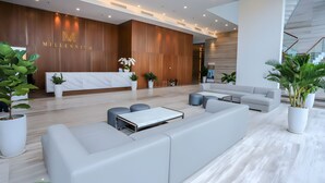 A modern lobby with a reception desk, seating area, and potted plants.