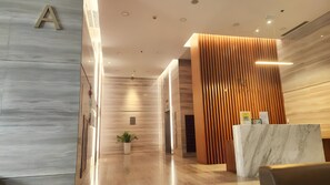 A modern reception area with a marble reception desk, wooden paneling, and a potted plant. - Luxury Millenium Apartment (Ho Chi Minh City)