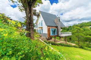 A house with a stone tower, a wooden deck, and a large tree in the foreground. - An Nhiên Villa (Lang Biang - Da Lat)