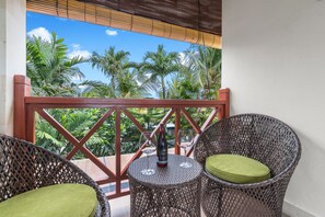 A balcony with wicker chairs, a table with a bottle and glasses, and a view of palm trees. - Luxurious, Spacious and Chic two bedroom villa in excellent location in Seminyak (Bali)