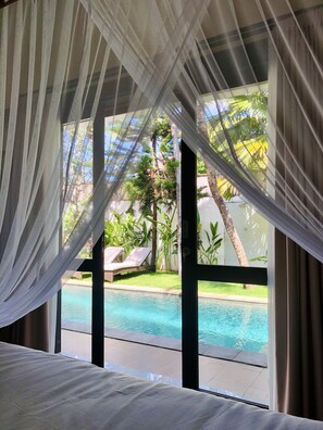 A room with a bed, a view of a swimming pool, and a balcony with plants and a chair. - Luxurious, Spacious and Chic two bedroom villa in excellent location in Seminyak (Bali)