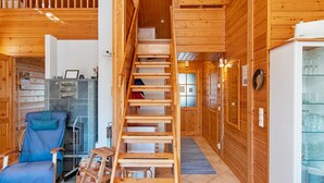Un interior de madera con una escalera central, una silla azul, una chimenea y un aparador de vidrio.