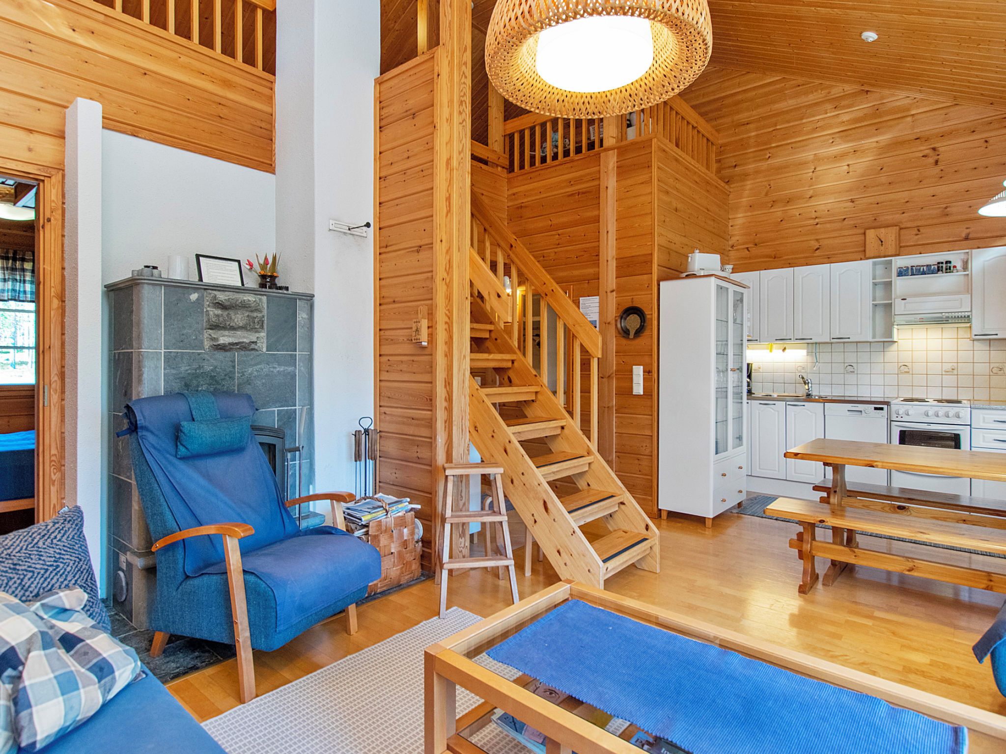 Un intérieur en bois avec un canapé bleu, une chaise en bois, un escalier et un coin cuisine.