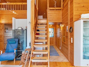Un intérieur en bois avec un escalier central en bois, une chaise bleue, une cheminée et un réfrigérateur.