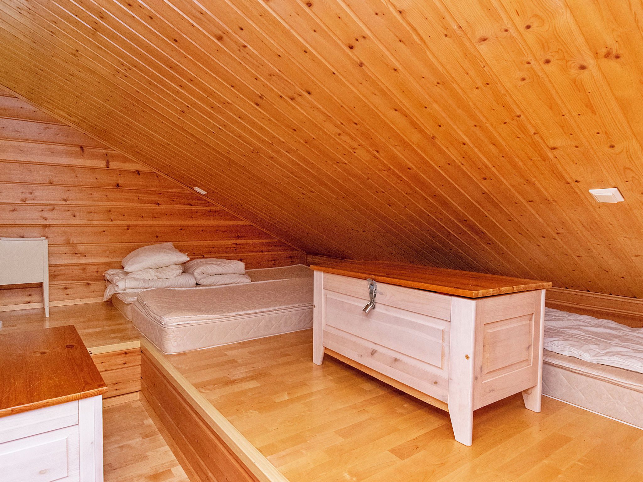A bedroom with a sloped ceiling, wooden walls, a bed, a dresser, and a nightstand.