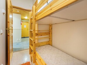 Habitación con literas de madera, un colchón blanco y una puerta visible que da a otra habitación.
